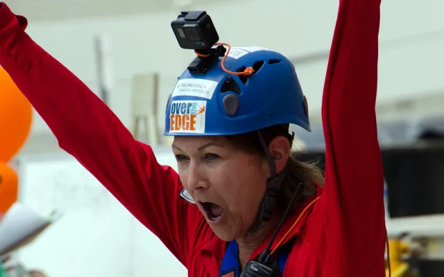Woman in blue helmet and red suit celebrates with arms raised.