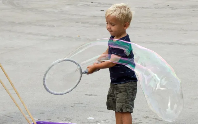 Young child making large bubble with a hoop outdoors.