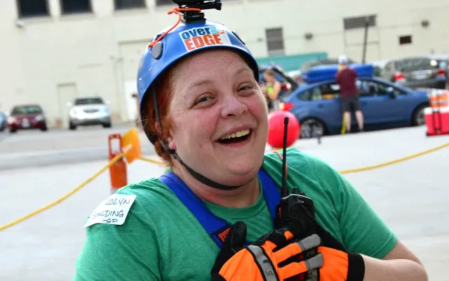 Woman in a helmet and harness, smiling outdoors.