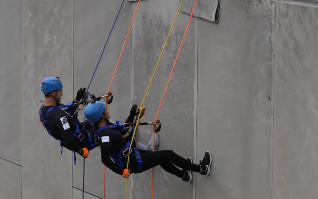 People rappelling down a building as others watch from the roof.