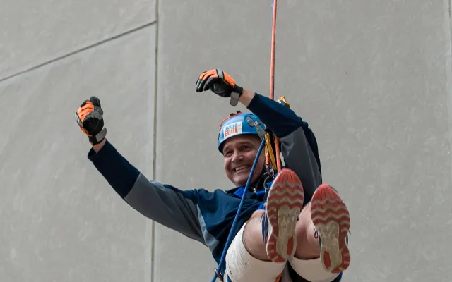 Person joyfully rappelling down a building wall.