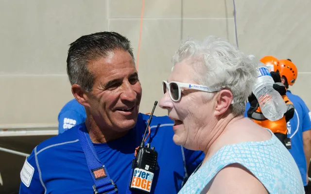 Man and woman smiling, wearing blue outfits and safety harnesses.