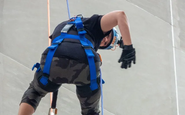 Climber in gear ascending a rope on a concrete wall.