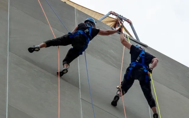 Two climbers in harnesses scaling a building.