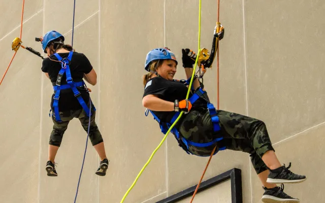 Two people in helmets rappelling down a building.