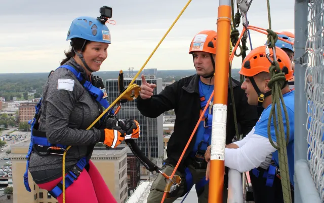 Woman in pink pants prepares to rappel down a building's side.