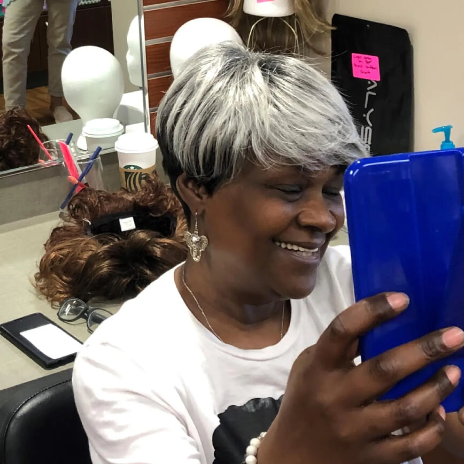 Smiling woman with short gray hair holding a blue tablet in a salon.